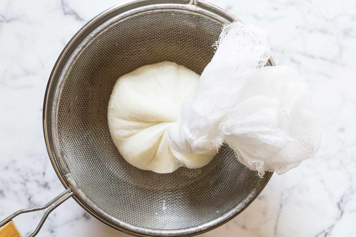Potato Latkes Recipe potatoes in cheesecloth in a sieve over a bowl