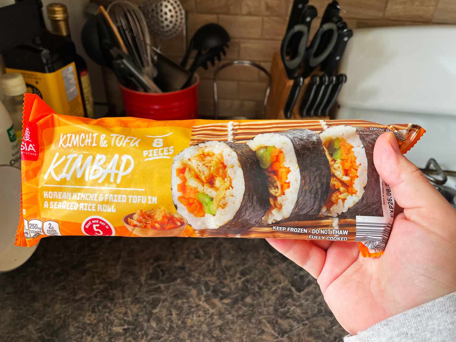 Package of kimchi and tofu kimbap held in a kitchen setting