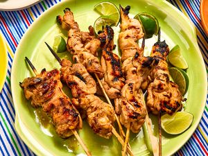 Grilled chicken satay skewers arranged on a plate with lime wedges