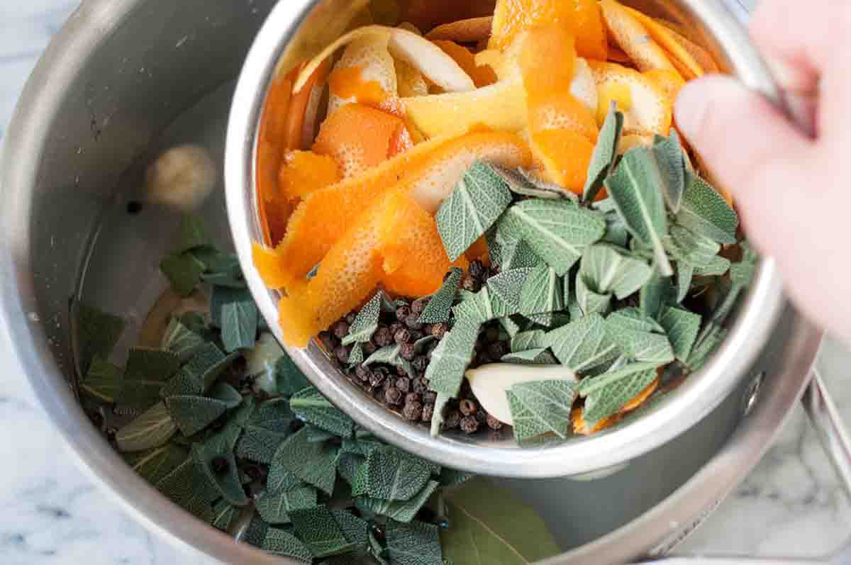 Herbs and orange peels going into a pot of water for brining