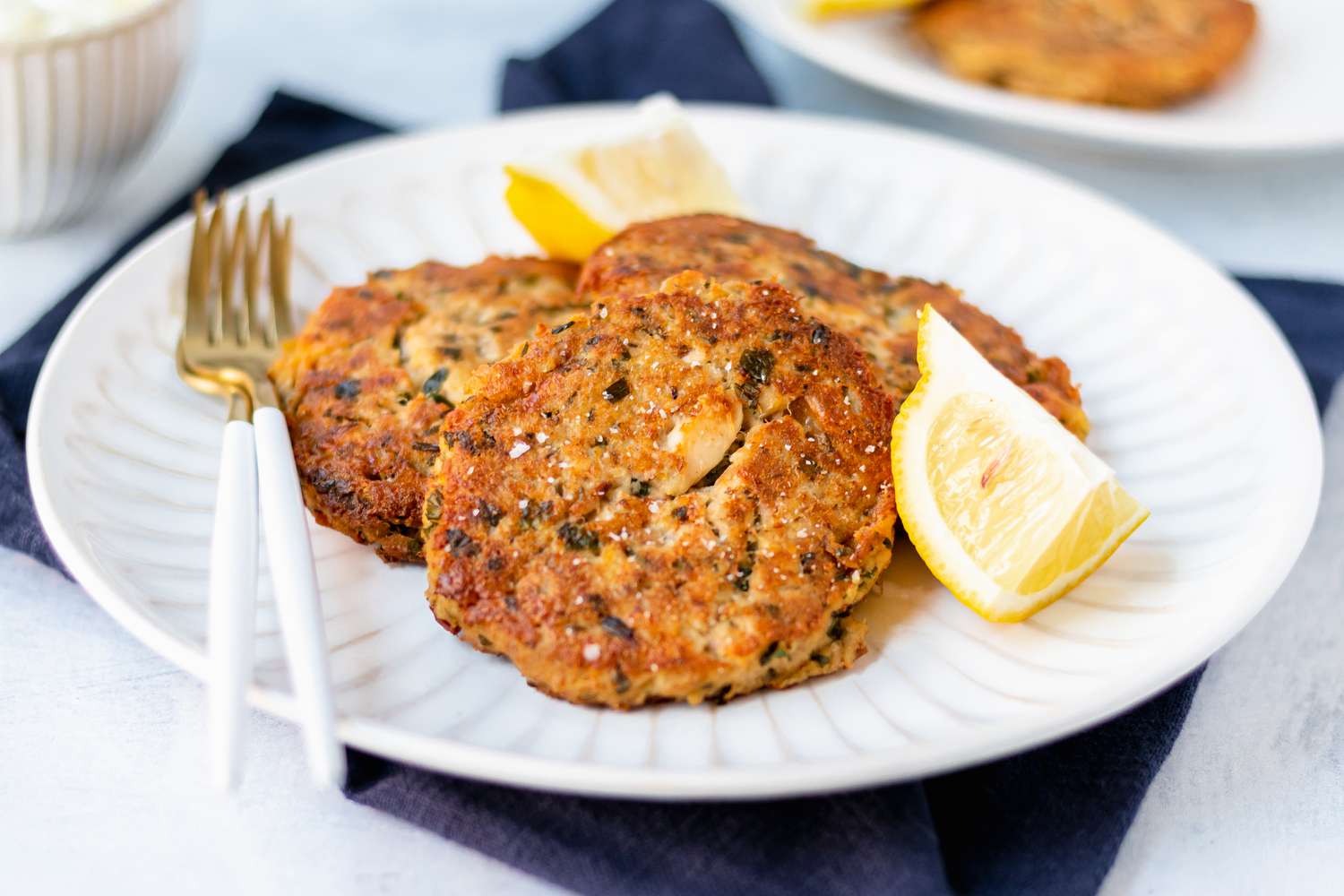 Tuna patties on a white plate along with a lemon wedge and fork.
