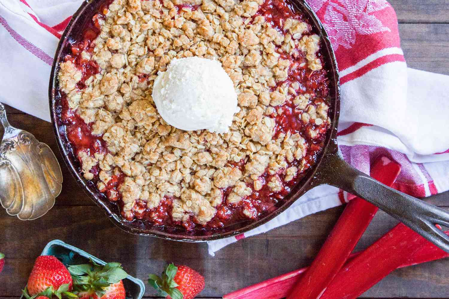 A skillet full of strawberry rhubarb crisp, with a scoop of vanilla ice cream on top