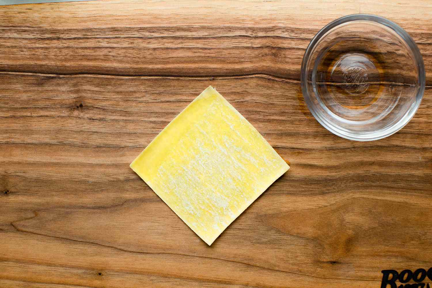 Pork and Chive Dumpling Wrapper (Square Wrapper) on a Counter Next to a Bowl of Water
