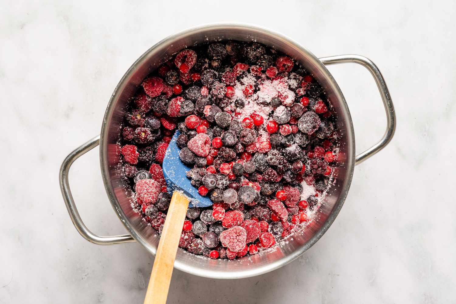 Overhead view of a metal pot and spatula with uncooked frozen berries and sugar for Easy British Summer Pudding recipe