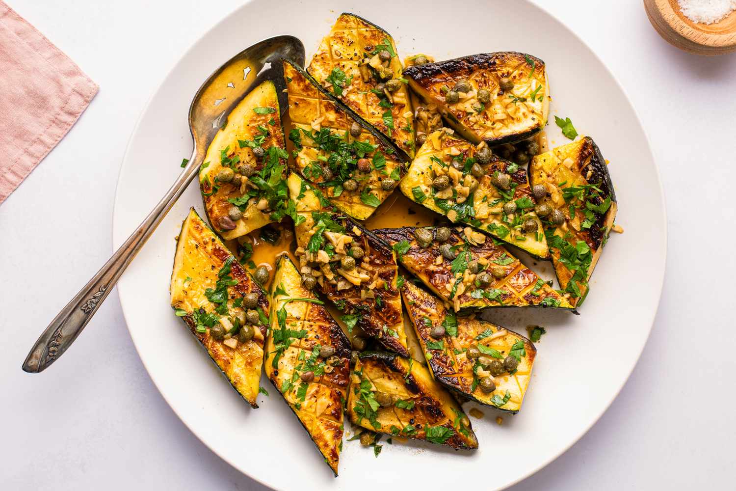 Sliced zucchini garnished with herbs on a white plate with a spoon