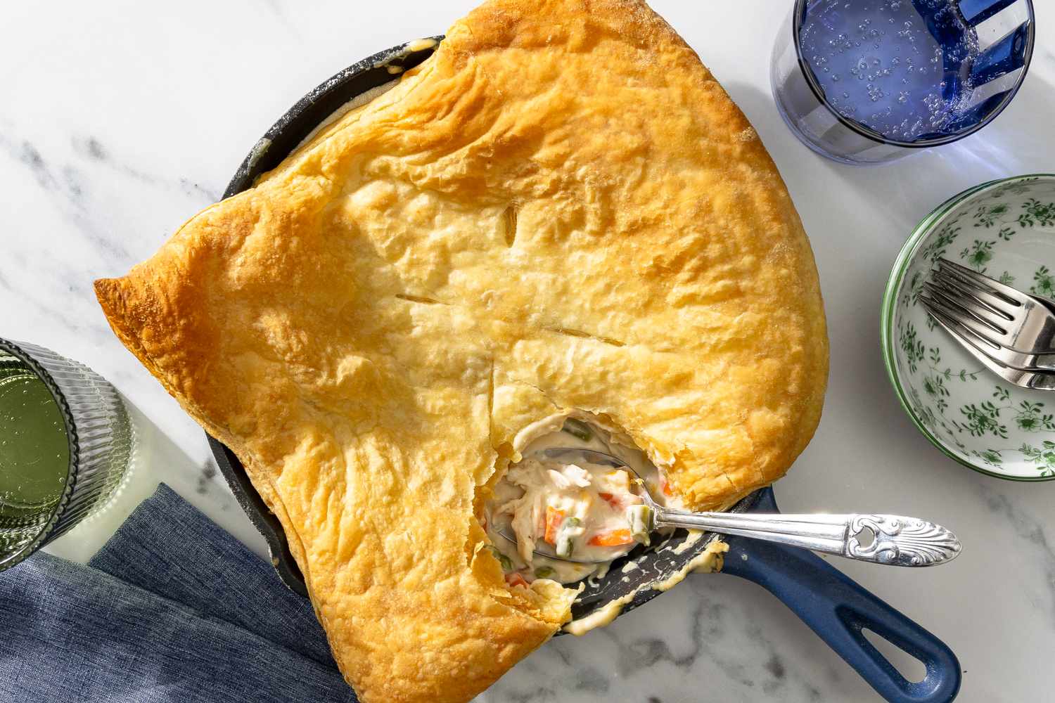 Chicken pot pie with a golden crust in a skillet and a serving spoon revealing the filling