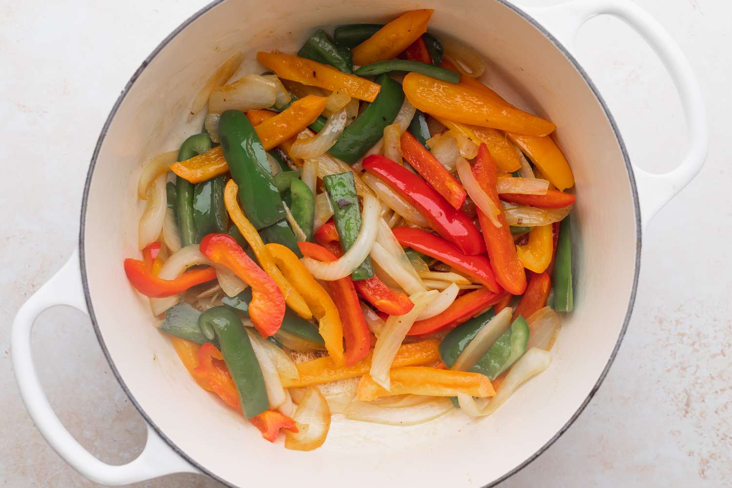 Sliced peppers and onions cooking in a dutch oven