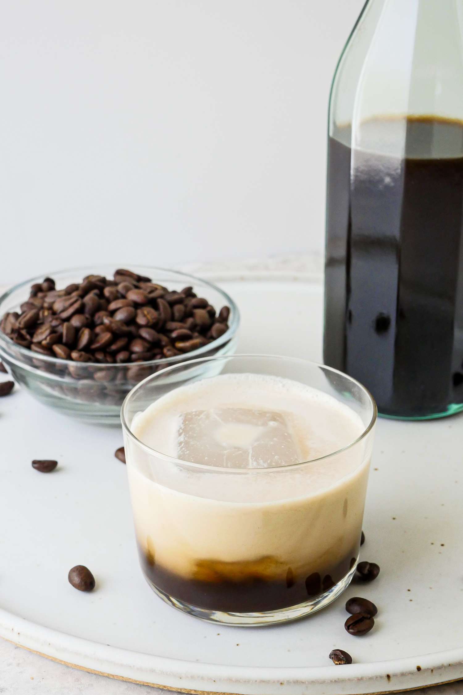 A white russian cocktail in front of a bowl of coffee beans and a bottle of Vegan Kahlua