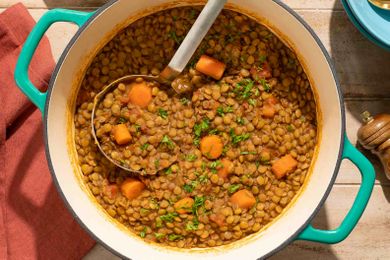A pot of spiced lentils with carrots garnished with greens and a serving spoon inside