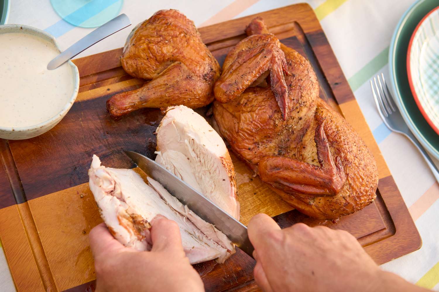 Carving a grilled half chicken on a cutting board, served with a side of sauce