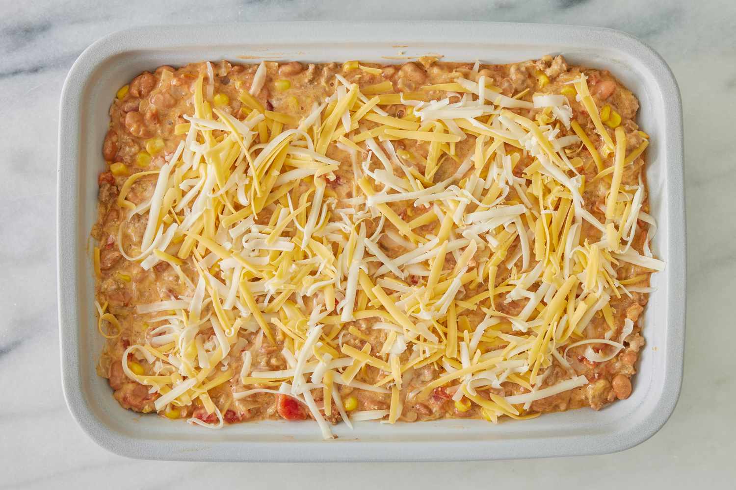 cowboy casserole filling added to a casserole dish and topped with shredded cheese