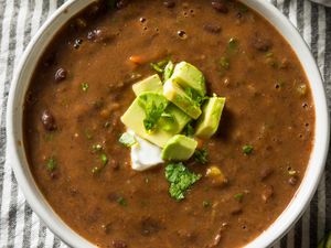 A bowl of bean soup garnished with chopped avocado cilantro and a dollop of sour cream
