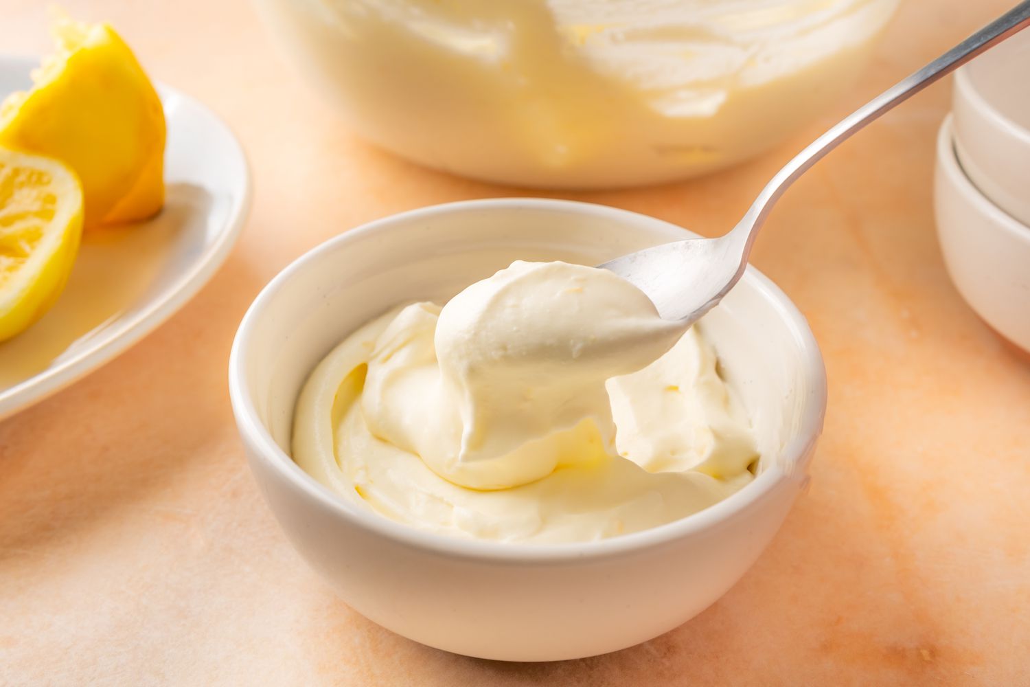 Angled view of a small white bowl of lemon mousse with a spoon on an orange surface