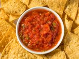A bowl of red salsa in the middle of a plate of corn chips