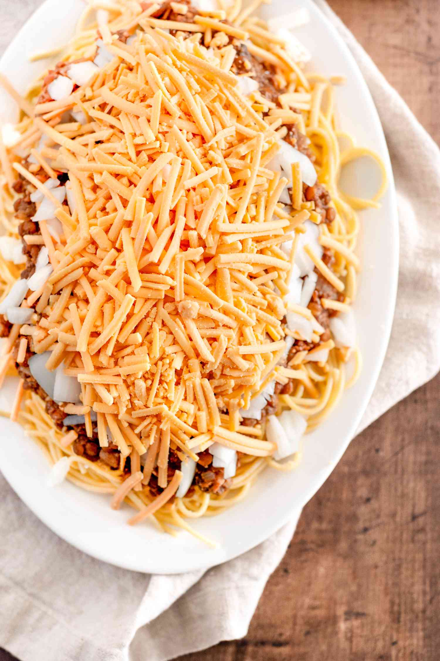 Vegan Cincinnati Chili Served over a Platter of Pasta and Topped with Cheese and Onions