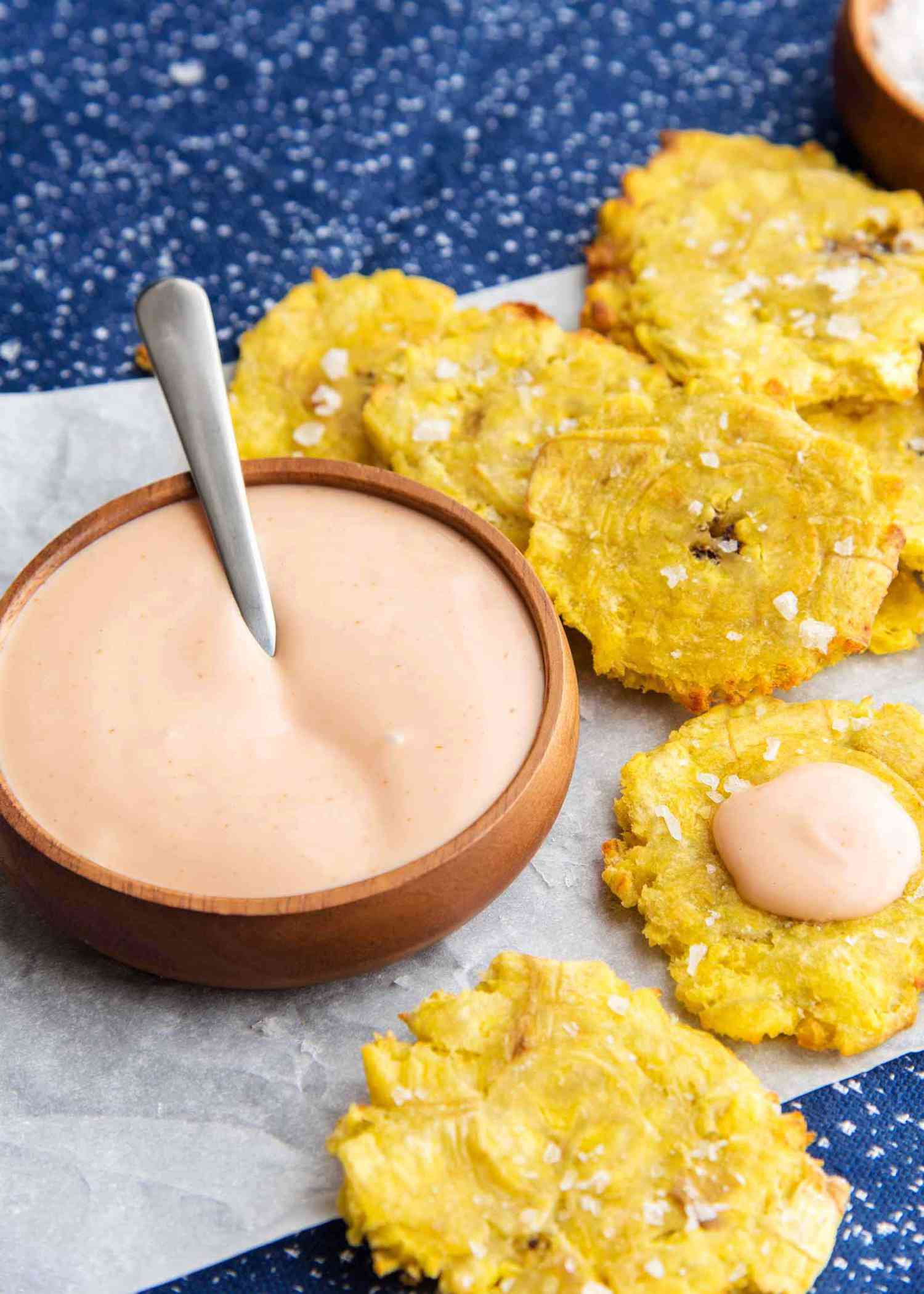 Air Fryer Tostones on parchment paper with a bowl of dip nearby.