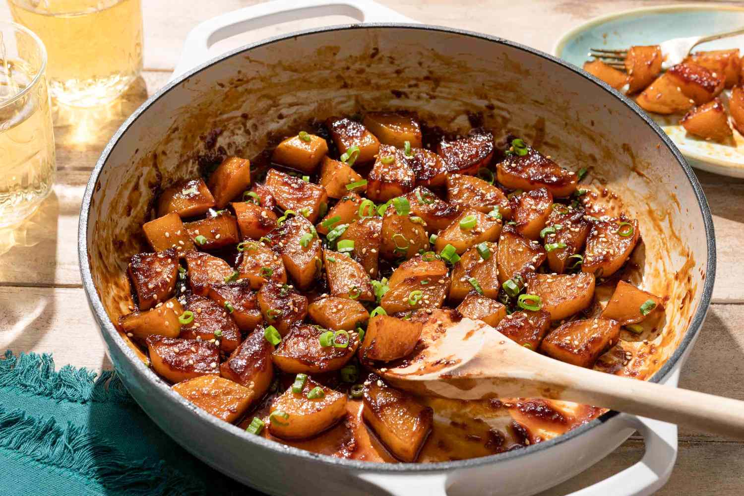 Braised potatoes in a pot with seasoning and garnish wooden spoon in view