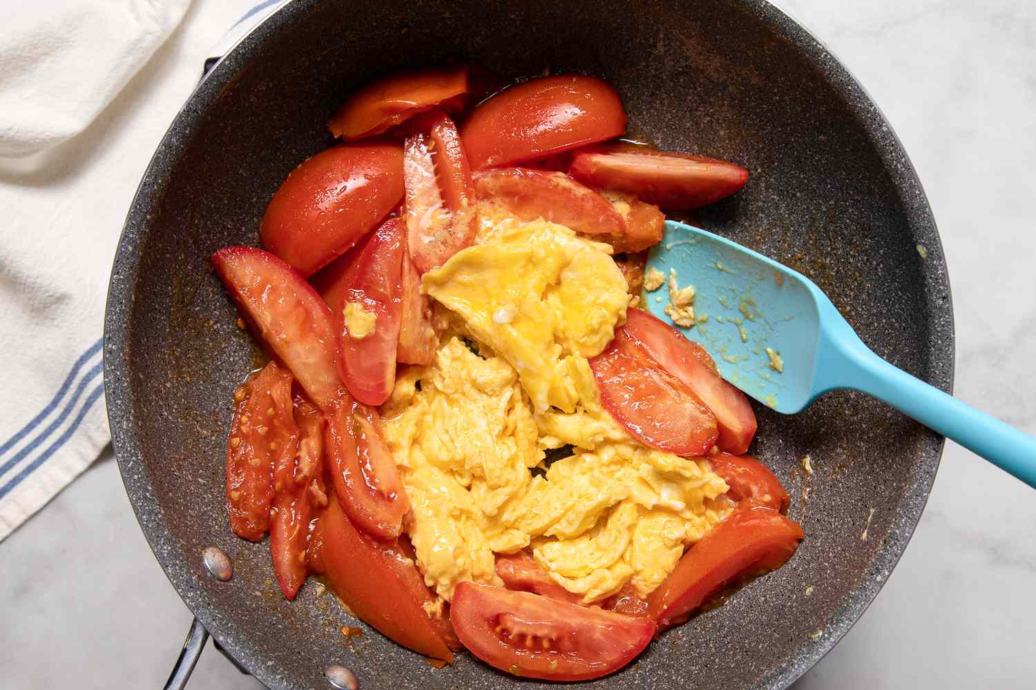 Adding scrambled eggs to a skillet with gently cooked tomatoes