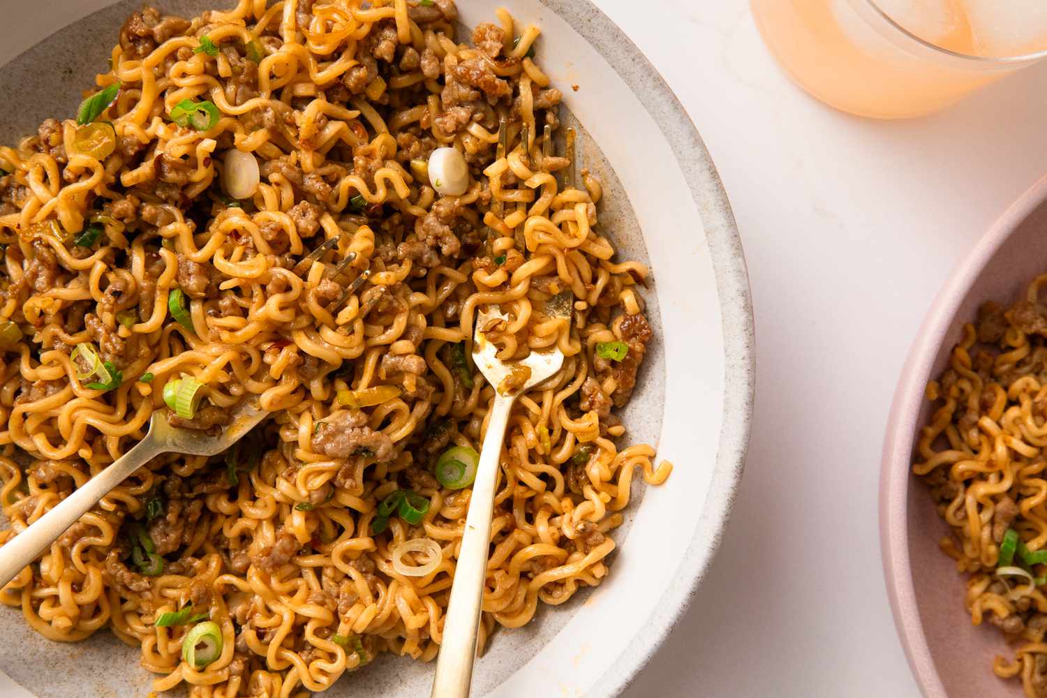 Overhead view of a large white bowl of pork and garlic noodles with two forks and topped with green onions